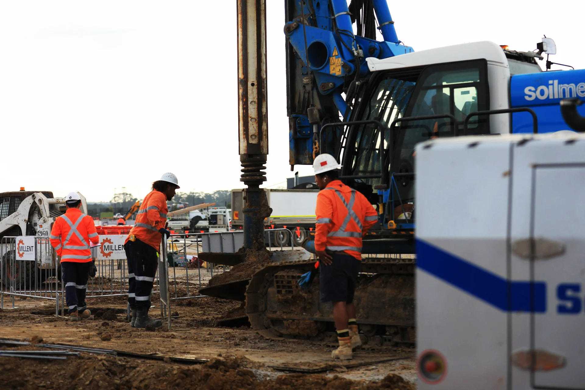 Construction workers in hi-vis clothing and hard hats supervising a Soilmec piling rig on site.