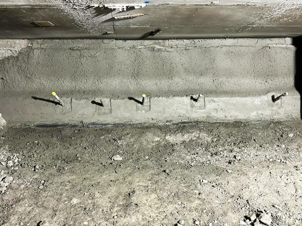 Close-up view of a shotcrete retaining wall featuring a row of protruding soil nails with protective caps.