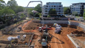 High-angle drone photo of a mobile concrete boom pump and agitator trucks conducting a slab foundation pour on an excavated construction site