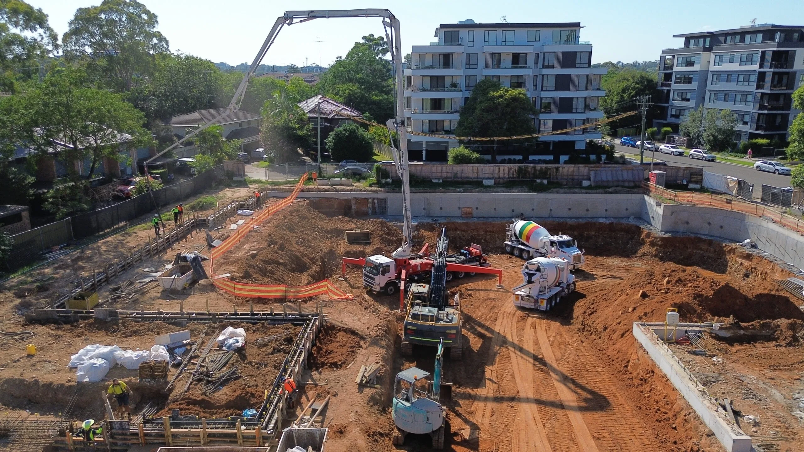 High-angle drone photo of a mobile concrete boom pump and agitator trucks conducting a slab foundation pour on an excavated construction site
