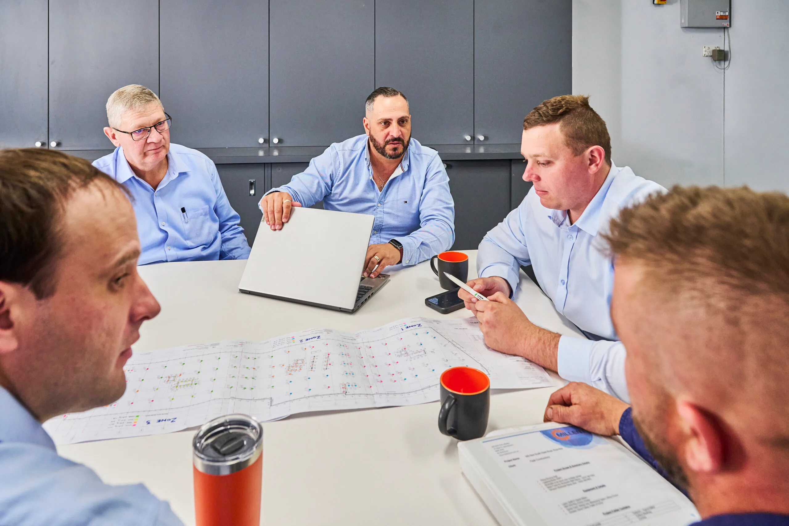 Civil engineering team and project managers reviewing architectural blueprints and digital plans around a boardroom table