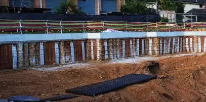 Excavated basement site showing a capping beam over contiguous piles lined with vertical strip filter drainage and steel reinforcement mesh prior to shotcreting.