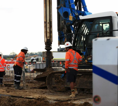 Construction workers in hi-vis clothing and hard hats supervising a Soilmec piling rig on site.