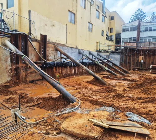 Inclined steel shoring props and soldier piles supporting a retaining wall on an excavation site.