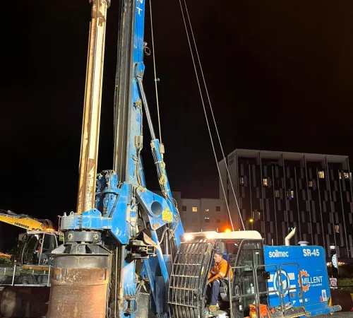A blue Soilmec SR-45 piling rig operating at night on an illuminated urban construction site.