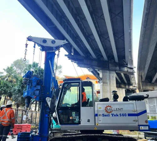 Profile view of a Soil Tek S60 piling rig drilling foundation bored piles underneath a concrete bridge deck.
