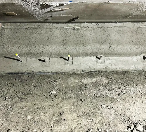 Close-up view of a shotcrete retaining wall featuring a row of protruding soil nails with protective caps.