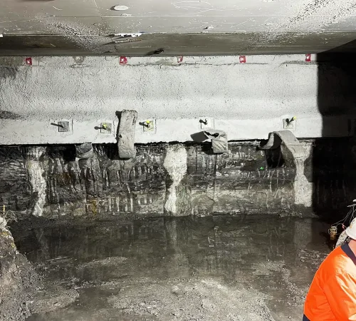 Shotcrete retaining wall with embedded soil anchors and a worker in hi-vis gear.