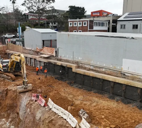 Anchored shoring wall Chatswood: piles, shotcrete panels and capping beam above an excavator and workers in hi-vis