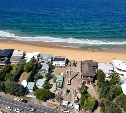 Aerial view of a piling rig and two excavators working in sand on the beachfront block, with the ocean beyond
