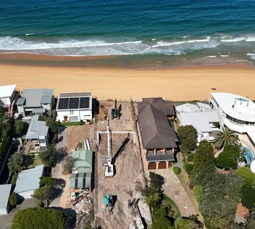 CFA piling Central Coast project: overhead view of a rig and excavators on a sandy beachfront block between two homes