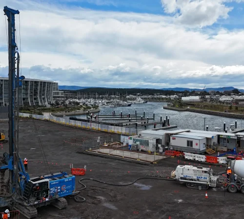 Piling rig, concrete pump and excavators working on the open Shell Cove site beside the marina